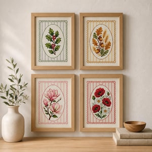 Puede incluir: Cuatro bordados en punto de cruz enmarcados con motivos botánicos: acebo con bayas rojas, bellotas con hojas de roble y trigo, flores de magnolia rosas y amapolas rojas con margaritas blancas, sobre fondos a rayas en marcos de madera clara.