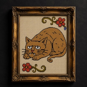 May include: A cross-stitch embroidery of a brown cat with white fangs and a grumpy expression, centered on a beige fabric background. The cat is flanked by two red flowers with green stems. The piece is enclosed in an ornate, antique gold frame.