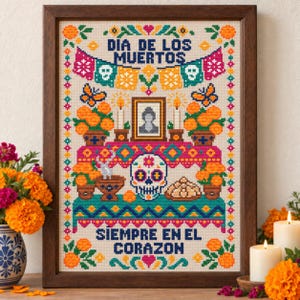 May include: A framed cross-stitch embroidery featuring a Dia de los Muertos altar with a central skull, marigold flowers, candles, and a framed portrait. The text reads DIA DE LOS MUERTOS and SIEMPRE EN EL CORAZON, surrounded by colourful geometric borders.