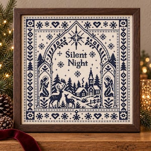 Puede incluir: Un bordado en punto de cruz enmarcado que muestra una escena invernal azul oscuro sobre tela color crema. El diseño incluye el texto "Silent Night" bajo una estrella, rodeado de ciervos, una iglesia, ángeles y bordes geométricos de copos.
