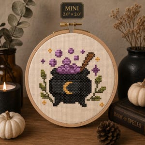 Puede incluir: Un bordado de punto de cruz en un bastidor de madera redondo con un caldero negro, una luna creciente amarilla, líquido morado burbujeante y follaje verde. El texto MINI 5,08 cm x 5,08 cm indica las dimensiones del diseño.