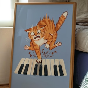 Könnte beinhalten: Ein gerahmter Kunstdruck mit einer Cartoon-Illustration einer orangefarbenen getigerten Katze mit weit aufgerissenen Augen, die auf Klaviertasten springt. Die Katze hat einen erschrockenen Ausdruck und kleine Notensymbole umgeben ihre Pfoten.