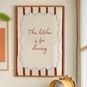 Könnte beinhalten: Ein rechteckiger Wandkunstdruck in einem Holzrahmen mit cremefarbenem Hintergrund und vertikalen dunkelroten Streifen. Ein hellblauer, wellenförmiger Rand umrahmt den mittigen Text "This kitchen is for dancing" in dunkelroter Schreibschrift.