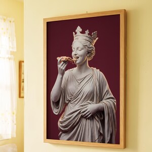 May include: A framed wall art print featuring a classical white marble-style statue of a crowned figure wearing draped robes, eating a slice of pizza against a solid deep burgundy background, enclosed in a light-toned wooden frame.