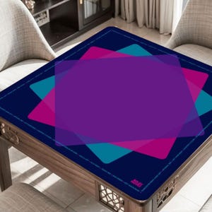 May include: A square table with a dark blue surface featuring overlapping geometric shapes in purple, teal, and pink. The table has a wooden frame and is surrounded by two chairs. The design includes text along the edge.