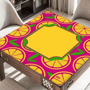 May include: A square table with a vibrant, colorful design. The tabletop features a repeating pattern of yellow lemon slices on a magenta background. A yellow central panel is framed by a green border. The table is made of wood.