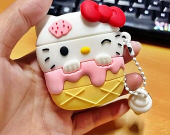 Könnte beinhalten: Ein weißes, rosa und gelbes Hello Kitty-Etui mit roter Schleife, das wie ein Eiswaffel aussieht. Das Etui hat eine kleine Kette mit einem weißen Anhänger. Das Etui wird in einer Hand gehalten.