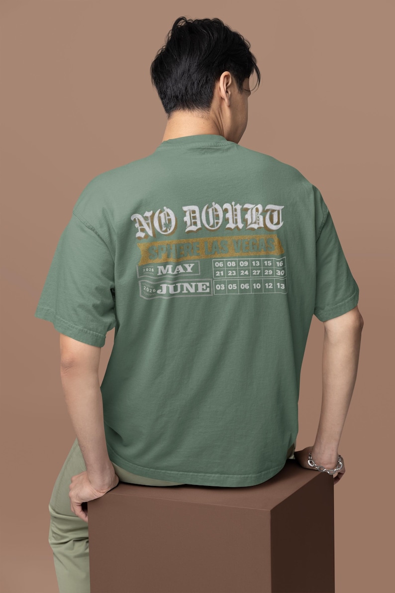May include: Sage green t-shirt with the text "NO DOUBT" in a vintage font. Below the text is a calendar grid for May and June 2020. The person is sitting on a brown cube.