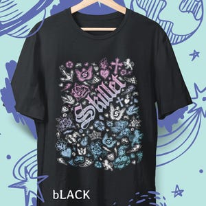 Peut inclure: T-shirt noir avec un motif graphique coloré représentant le mot "Skillet" dans une police stylisée, entouré de diverses illustrations dans des tons de rose et de bleu. Le mot "BLACK" est imprimé en bas.