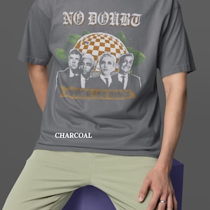 May include: Charcoal gray t-shirt featuring the band No Doubt with a graphic of the band members and the text "SHOWS IN LAS VEGAS". The shirt is a short-sleeved, crew neck style.