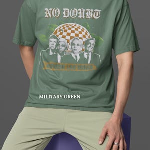 May include: Military green t-shirt featuring the band No Doubt with a checkered globe graphic and the text "Where the Vegas". The shirt is a crew neck and the text "Military Green" is printed below the graphic.