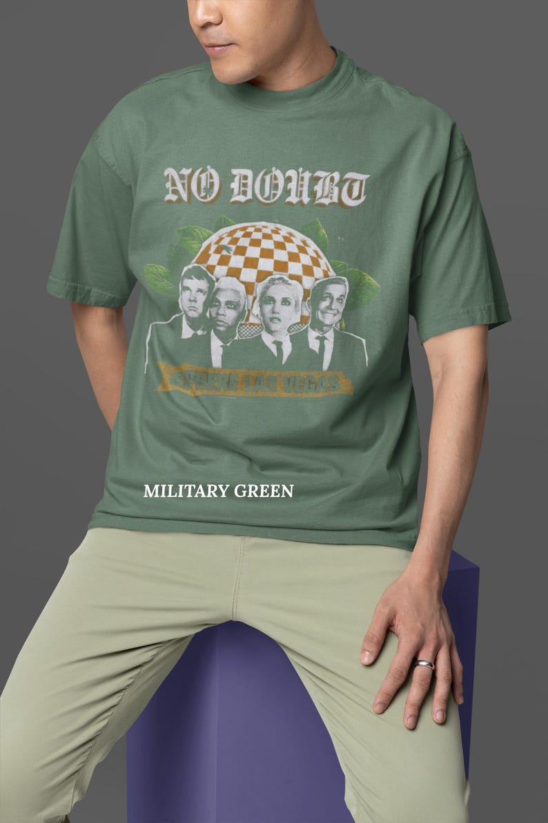 May include: Military green t-shirt featuring the band No Doubt with a checkered globe graphic and the text "Where the Vegas". The shirt is a crew neck and the text "Military Green" is printed below the graphic.