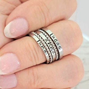 May include: Four silver stacking rings with the names "Lucas", "Anna", "Liam", and "Ava" engraved on them.