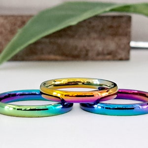 May include: Three thin rainbow-colored metal rings stacked on top of each other. The rings are a gradient of colors, starting with yellow and ending with purple.