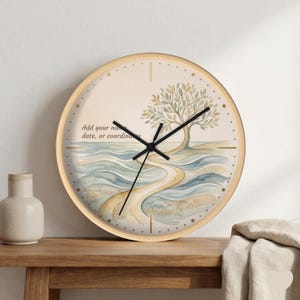 May include: A round wall clock with a light wood frame. The clock face features a watercolor painting of a tree and a path winding through water. The text "Add your name, date, or coordinates" is printed on the clock face.