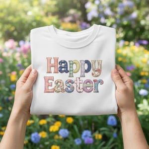 May include: A white crew neck sweatshirt with the words "Happy Easter" in colorful, patterned letters. The letters have floral, plaid, and polka dot designs. The sweatshirt is held up by two hands against a background of flowers.