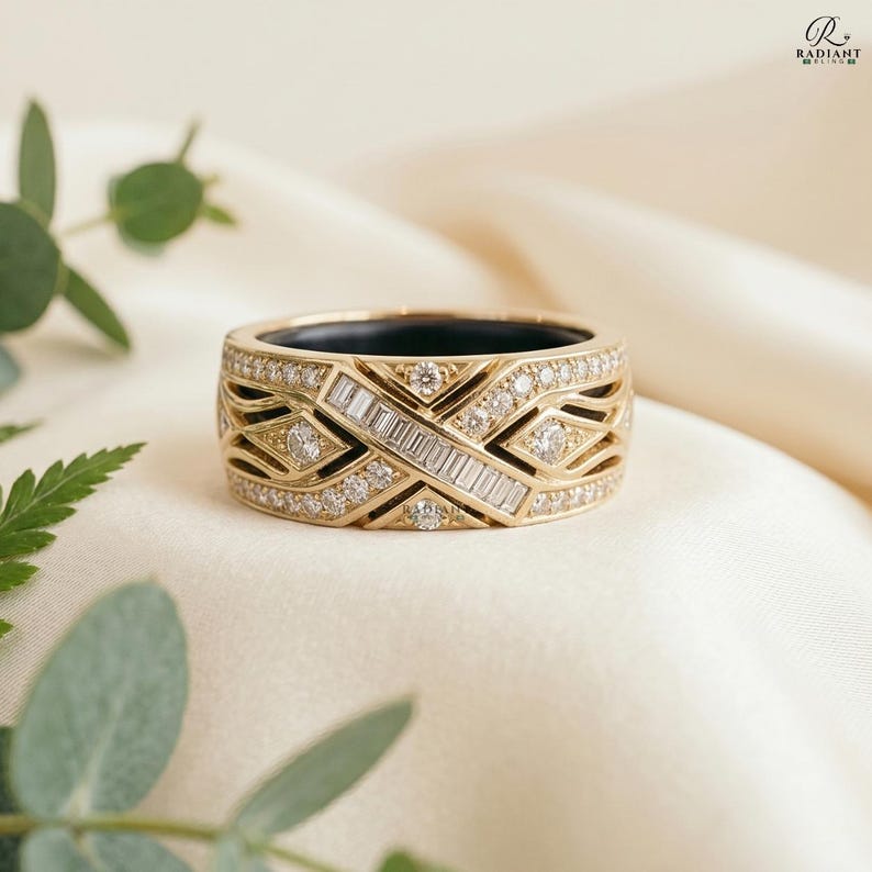 Close-up of a 14K gold Oura Ring Gen 4 cover featuring a geometric criss-cross design with baguette and round lab-grown diamonds, resting on soft cream fabric with green botanical leaves.