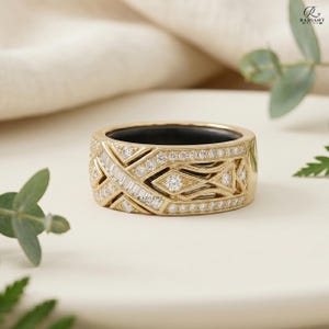 Upright view of a thick 14K gold geometric diamond ring guard, clearly showing the inner black band of a smart ring. The jewelry is displayed on a matte cream surface in a soft, natural setting.