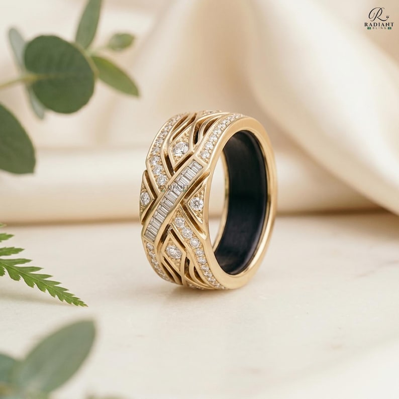 Angled view of a luxurious 14K gold smart ring jacket with pave diamonds and a baguette diamond center, encasing a black Oura ring. The ring sits on a smooth ivory surface surrounded by eucalyptus sprigs.