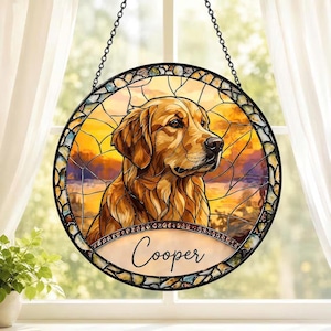 May include: A circular stained glass suncatcher featuring a golden retriever portrait against a warm sunset background. The piece is framed in black metal with a decorative border and includes a black hanging chain. The name Cooper is written in black script at the bottom.
