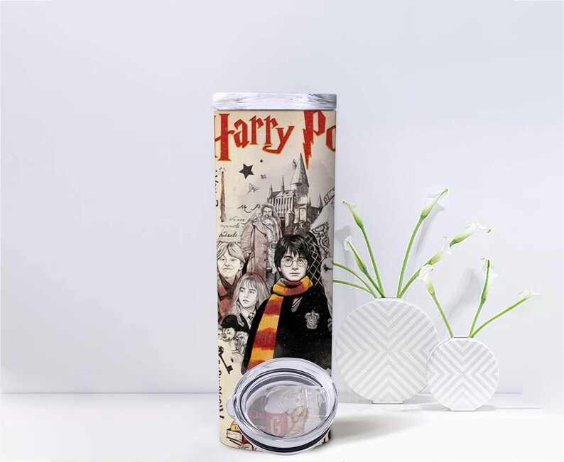 May include: A stainless steel tumbler featuring a design from the Harry Potter series. The design includes the words "Harry Potter" in red, along with illustrations of characters and Hogwarts castle. The tumbler has a silver lid and a clear base.