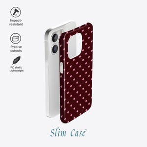 Puede incluir: Una funda de tel&eacute;fono burdeos con un patr&oacute;n de peque&ntilde;os corazones rosas. La funda se muestra junto a un tel&eacute;fono plateado, con las palabras "Slim Case" en una fuente cursiva en la parte inferior. Resistente a impactos y ligera.