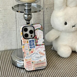May include: A decorative phone case with a floral and inspirational design. The case features the words "grace", "let your light shine", and "God is good all the time". The case has a white background with pink, yellow, and blue floral accents.