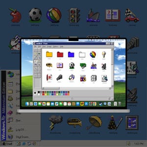 May include: A laptop screen displaying a Windows Millennium Edition desktop interface with a classic Paint window open. The window contains a grid of colorful pixel-art icons, including folders, a soccer ball, a boat, and a trumpet, over a green hill wallpaper.