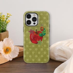May include: A phone case with a red apple and a green and red caterpillar illustration. The case has a green polka dot background and a star design. The phone case is designed for a smartphone.