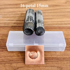 May include: Two metal tools with a 16-petal design, labelled "16-petal 15mm", are positioned above a clear plastic case. A square copper piece below shows the stamped floral pattern. These tools are for metalworking and crafting.