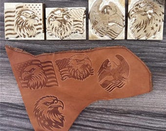 May include: A collection of wood stamps and a piece of brown leather, all featuring detailed carvings of American eagles and flags. The stamps are square, while the leather piece displays various eagle designs.