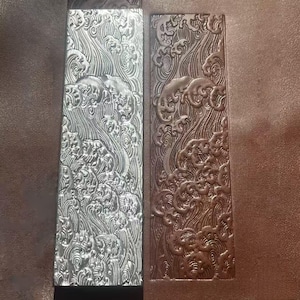 May include: Two rectangular panels with a detailed relief design. One panel is silver, the other is bronze. The relief depicts stylized waves and clouds, creating a textured surface. The panels are likely decorative elements.