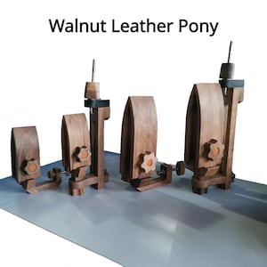 Pode incluir: Quatro ponies de couro de nogueira de tamanhos variados. Cada um apresenta uma estrutura de madeira, um mecanismo de fixação e um poste central. O texto "Walnut Leather Pony" está no topo da imagem.
