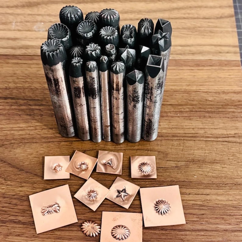 May include: A selection of metal stamping tools with diverse decorative patterns. The tools are cylindrical with textured ends. Several stamped copper squares with floral and geometric designs are also shown.