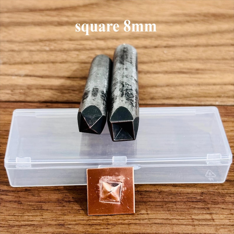 May include: Two metal square punches, each 8mm, with a clear plastic case and a copper square with a stamped square design. The punches are dark grey and have a square end. The text "square 8mm" is above the punches.