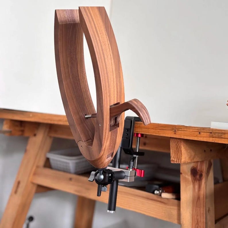 K&ouml;nnte beinhalten: Ein h&ouml;lzerner Holzbearbeitungsschraubstock mit geschwungenem Design, an einer h&ouml;lzernen Werkbank befestigt. Der Schraubstock ist aus dunkelbraunem Holz gefertigt und hat eine Metallklemme und Einstellkn&ouml;pfe. Die Werkbank ist ebenfalls aus Holz.