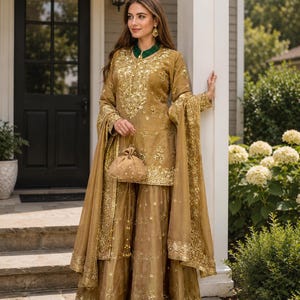 Peut inclure: Un ensemble tunique à manches longues et pantalon large de couleur dorée, orné de broderies dorées complexes et de sequins. La tenue comprend un dupatta doré transparent assorti et un petit sac à main rond à cordon avec des perles.