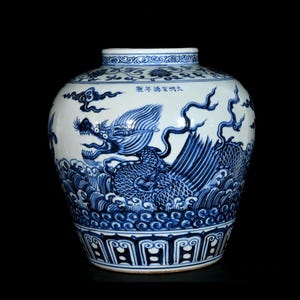 Könnte beinhalten: Ein weißes Porzellangefäß mit handgemalten blauen Unterglasurmotiven, die einen Drachen inmitten von wirbelnden Wolken und brechenden Wellen zeigen. Auf der Schulter befinden sich chinesische Schriftzeichen 大明宣德年製 und ein dekorativer Rand am Boden.