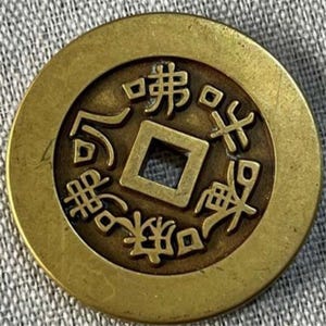 May include: A round, antique brass coin with a square hole in the center. The coin features intricate Chinese characters around the central square. The coin has a worn, aged appearance, suggesting it is an antique.