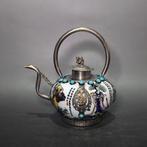 Wijnkan van wit porselein met een schoonheidsfiguur, omwikkeld met verzilverd koper en ingelegde turkooizen edelstenen.