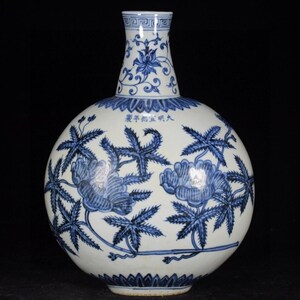 Puede incluir: Un jarrón de porcelana redondo con cuello estrecho, con patrones florales y de hojas en azul bajo vidriado sobre fondo blanco. El cuello muestra un borde geométrico, el cuerpo incluye caracteres chinos cerca de la parte superior y pétalos en la base.
