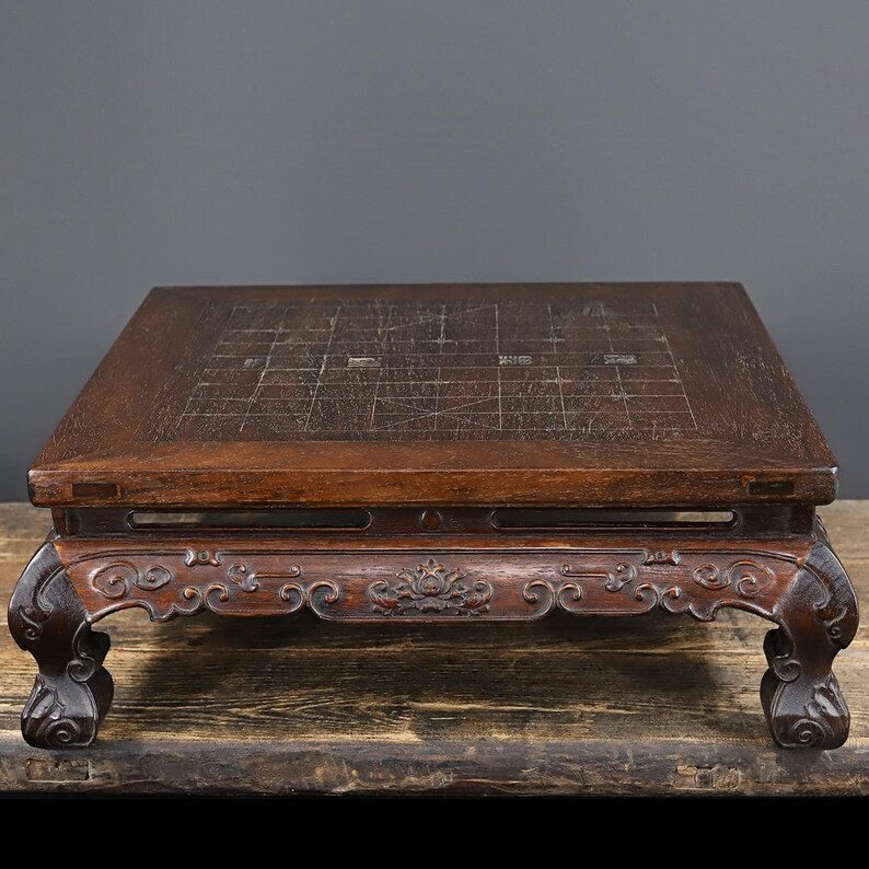 May include: A dark brown wooden board game table featuring a square top with an etched grid pattern and Chinese characters. The table is supported by four ornate, curved legs with intricate carved details along the apron and base edges.