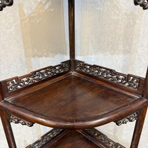 May include: A dark brown wooden corner shelf unit featuring multiple tiers with curved edges. Each shelf is framed by intricate, openwork carved lattice detailing along the back edges and decorative scrollwork supports beneath the shelf surfaces.