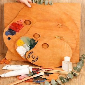Può includere: Palette di legno per artisti di varie dimensioni, alcune con macchie di vernice. Le palette hanno un foro per il pollice e un emblema decorativo. Sono presenti anche tubetti di vernice, pennelli e una piccola bottiglia.
