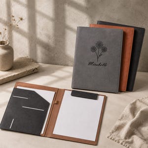May include: A set of three rectangular document folders in grey, tan, and black. The grey folder features a black line drawing of three daisies and the name Mirabelle. One tan folder is open, revealing a black document pocket and a white paper.