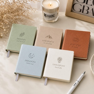 Puede incluir: Cinco cuadernos pequeños y texturizados en verde salvia, beige, terracota, azul claro y crema. Cada uno presenta un icono y texto únicos: BREATHE and be still, FIND BEAUTY in everyday, STAY WILD at heart, DREAM BIG little one y LIVE GENTLY live fully.