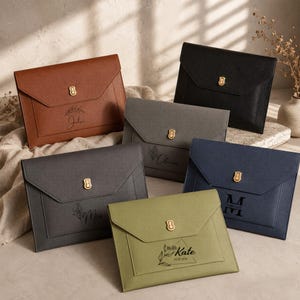 May include: A collection of six envelope-style document folders in various colours including brown, black, grey, navy blue, and olive green. Each folder features a gold-toned metal clasp closure and is personalised with names and floral designs.