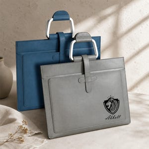 May include: A blue and a grey rectangular document case, each featuring a silver metal handle and a vertical strap closure. The grey case displays a black graphic of a lion head inside a shield crest above the printed text Abbott.