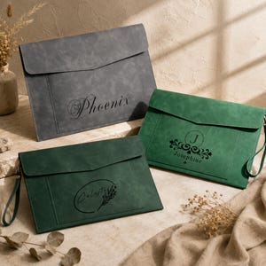 Puede incluir: Tres carpetas rectangulares para documentos con solapas y correas de muñeca. Una es gris con el nombre Phoenix, una es verde con el nombre Josephine y un emblema floral, y una es verde oscuro con el nombre Celeste y un diseño floral.