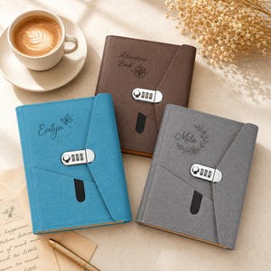 May include: Three fabric-covered journals with combination locks in blue, brown, and gray. The blue journal features the name Evelyn and a butterfly, the brown one says Adventure Book with a compass, and the gray one features the name Mila.